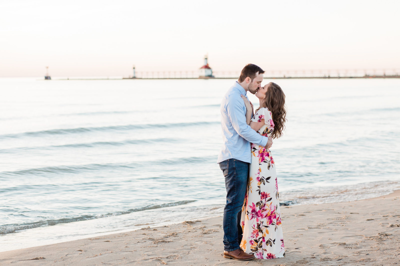 A couple kissing in front of a lighthouse at their Silver Beach engagement session.